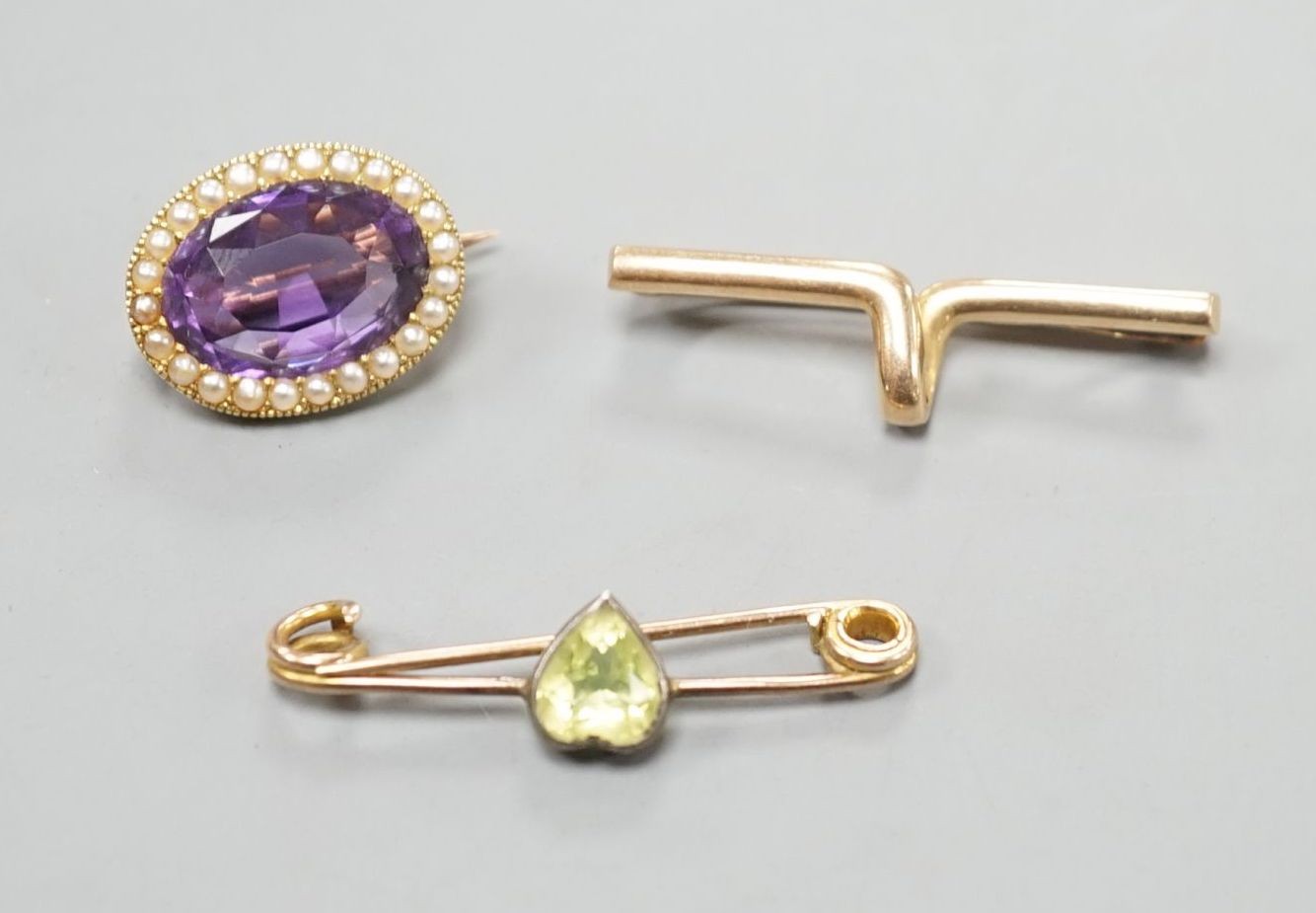 A yellow metal cravat pin, 37mm, a 9ct and heart shaped gem set bar brooch and a yellow metal, amethyst and seed pearl set oval brooch, gross weight 10.4 grams.